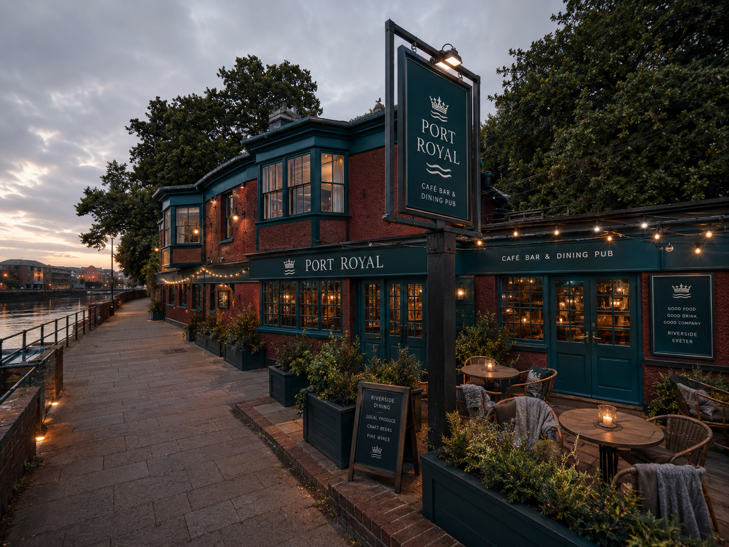 The Port Royal riverside pub in Exeter at dusk, with warm lit windows and terrace seating beside the River Exe